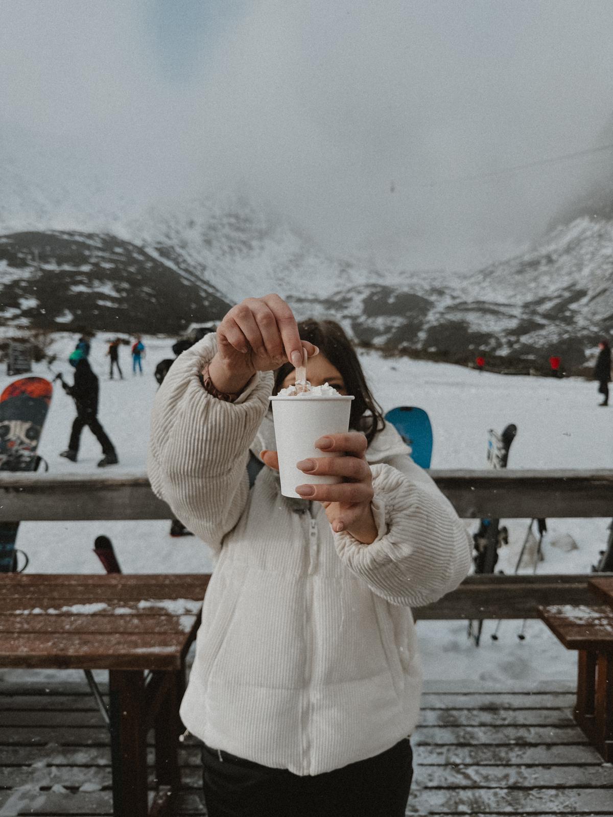 Zwei bunte Cocktails in der Hand, mit Blick auf einen sonnigen Strand und das glitzernde Meer – pure Entspannung im tropischen Paradies.
